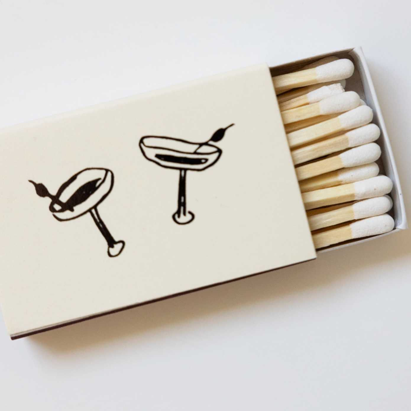 off white matchbox half open to reveal white matches. illustrated black martini glasses are on the matchbox