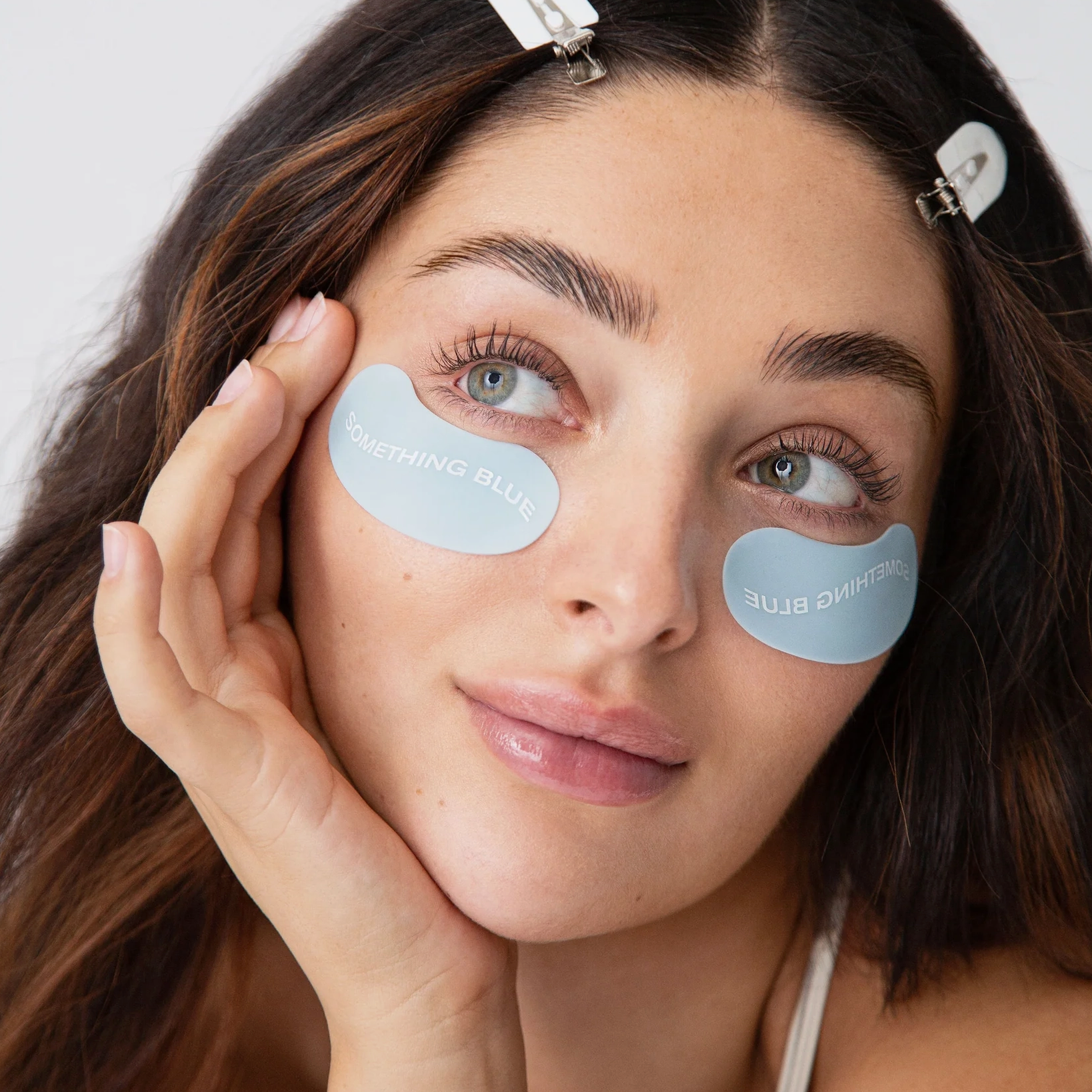 close up of womans face wearing light blue eye masks under her eyes. the masks say SOMETHING BLUE in white letters. 