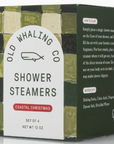 A close-up of a stack of four white shower steamers next to a box labeled "Old Whaling Co Shower Steamers" in the fragrance "Coastal Christmas." The box features a white label with a whale logo and green, black, and gold textured design elements.