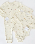 A matching baby clothing set consisting of a cream-colored long-sleeve onesie and a footed one-piece sleeper, both with whimsical mushroom and forest-themed prints. The outfits are laid flat on a white background, with small brand tags attached.