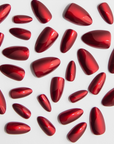 A collection of glossy, metallic red press-on nails of varying sizes scattered on a white surface. The nails are almond-shaped with a reflective finish, creating a sleek and polished look.