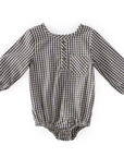 A long-sleeved baby romper made from black-and-white gingham fabric, featuring a front button placket, a small chest pocket, and elasticated leg openings for a comfortable fit.