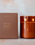 BROWN BOX LABELED: "BOTANICA SPICED GINGER HOLIDAY EDITION." THE CANDLE IS NEXT TO THE BOX AND IS ORANGE IN COLOR.