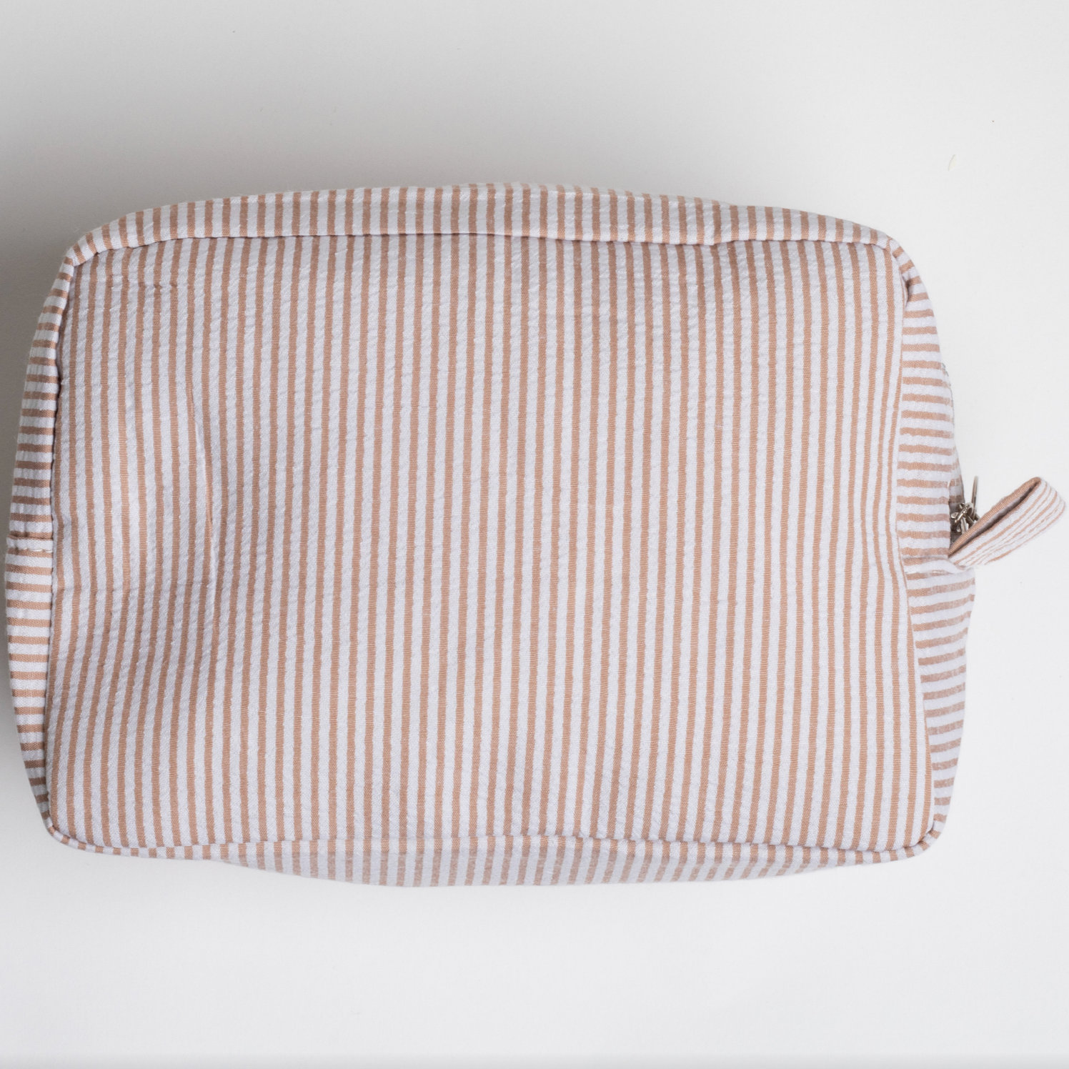 This image shows a rectangular pouch or toiletry bag with a soft, padded structure. It features a light tan and white striped pattern, with a zipper closure visible on one side, along with a small fabric loop near the zipper pull. The pouch is placed on a plain white background.
