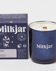 navy blue box that says MILKJAR ORIGINAL PATTIE VANILLA CHAI & PEPPERMINT SCENTED COCONUT SOY CANDLE. next to blue candle with wooden wick that says milkjar on it. 