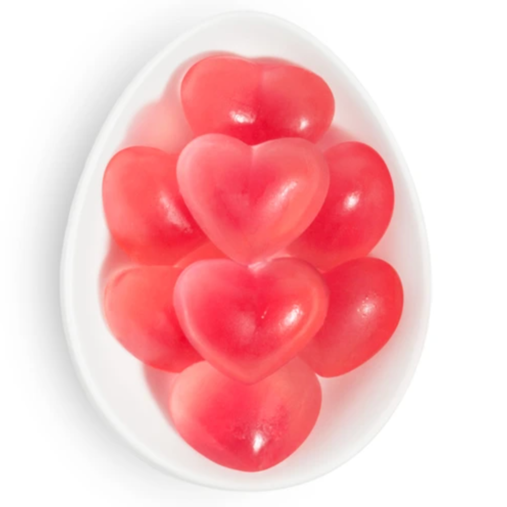 A close-up view of a white, oval dish filled with red and pink heart-shaped gummies. The gummies have a glossy texture, creating a soft and translucent appearance, symbolizing sweetness and affection.