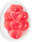 A close-up view of a white, oval dish filled with red and pink heart-shaped gummies. The gummies have a glossy texture, creating a soft and translucent appearance, symbolizing sweetness and affection.