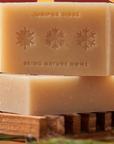 THE SOAP IS DISPLAYED AND ENGRAVED IN IT IS "JUNIPER RIDGE BRING NATURE HOME" WITH SNOWFLAKES. THE BACKGROUND IS RED AND THE SOAP SITS ON WOOD 