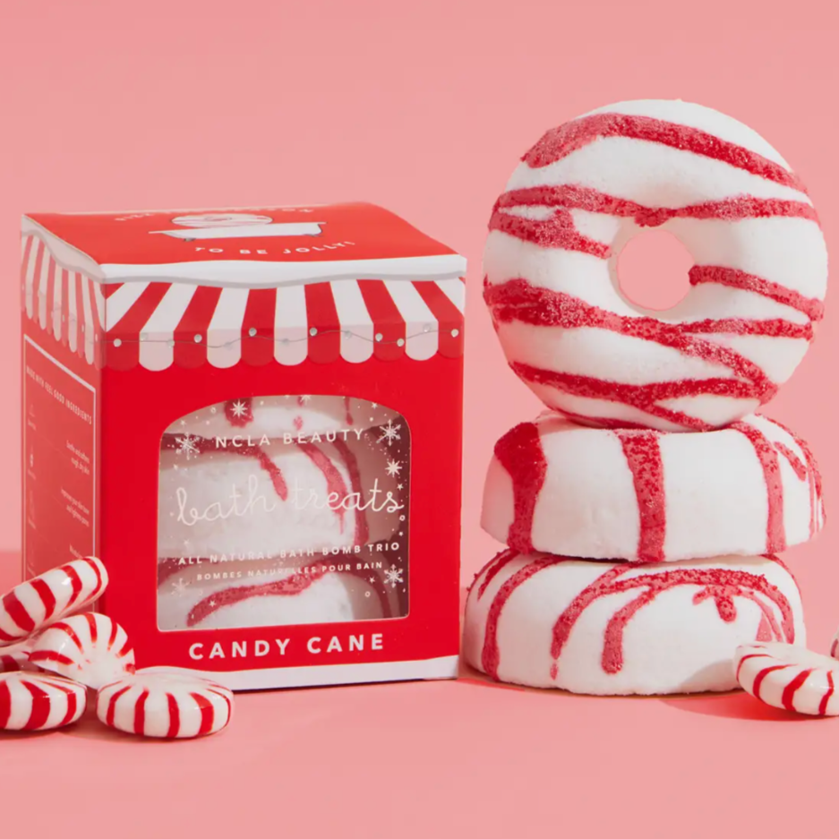 NCLA BEAUTY WRITTEN IN WHITE IN RED CHRISTMAS PACKAGING. THE ITEM IS A WHITE BATH TREAT WITH RED STRIPES ON A PINK BACKGROUND
