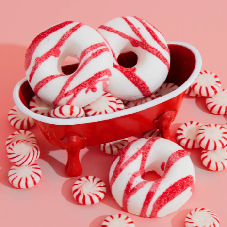 RED AND WHITE STIPE BATH TREATS IN A MINI RED BATHTUB NEXT TO PEPPERMINT CANDIES ON A PINK BACKGROUND