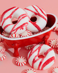 RED AND WHITE STIPE BATH TREATS IN A MINI RED BATHTUB NEXT TO PEPPERMINT CANDIES ON A PINK BACKGROUND