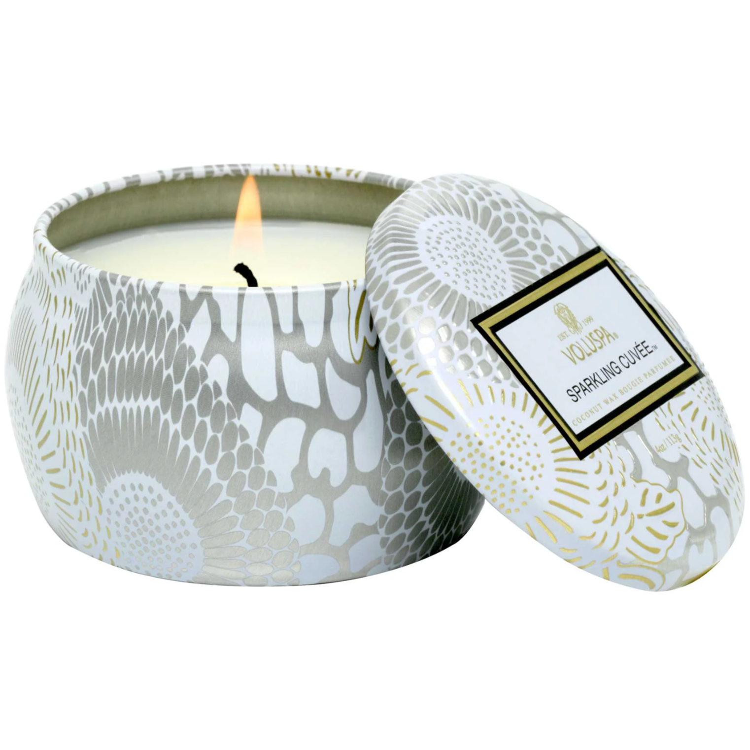 WHITE, SILVER AND GOLD COLORED CANDLE DISPLAYED OPEN WITH IT LIT. THE SCENT IS SPARKLING CUVEE