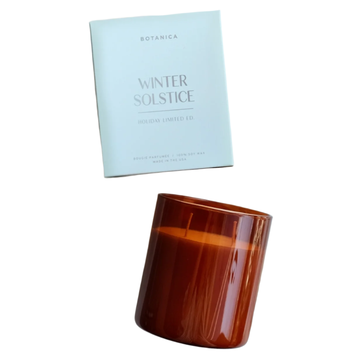 The image shows a candle product from the brand "Botanica" with the label "Winter Solstice" and "Holiday Limited Ed" on the packaging. The packaging is a simple, light-colored box with minimalist text, conveying a calm and festive feel. The candle is in a warm amber-colored glass container and is placed next to the box on white background. This setup enhances the candle's luxurious and cozy aesthetic, creating an inviting winter ambiance.
