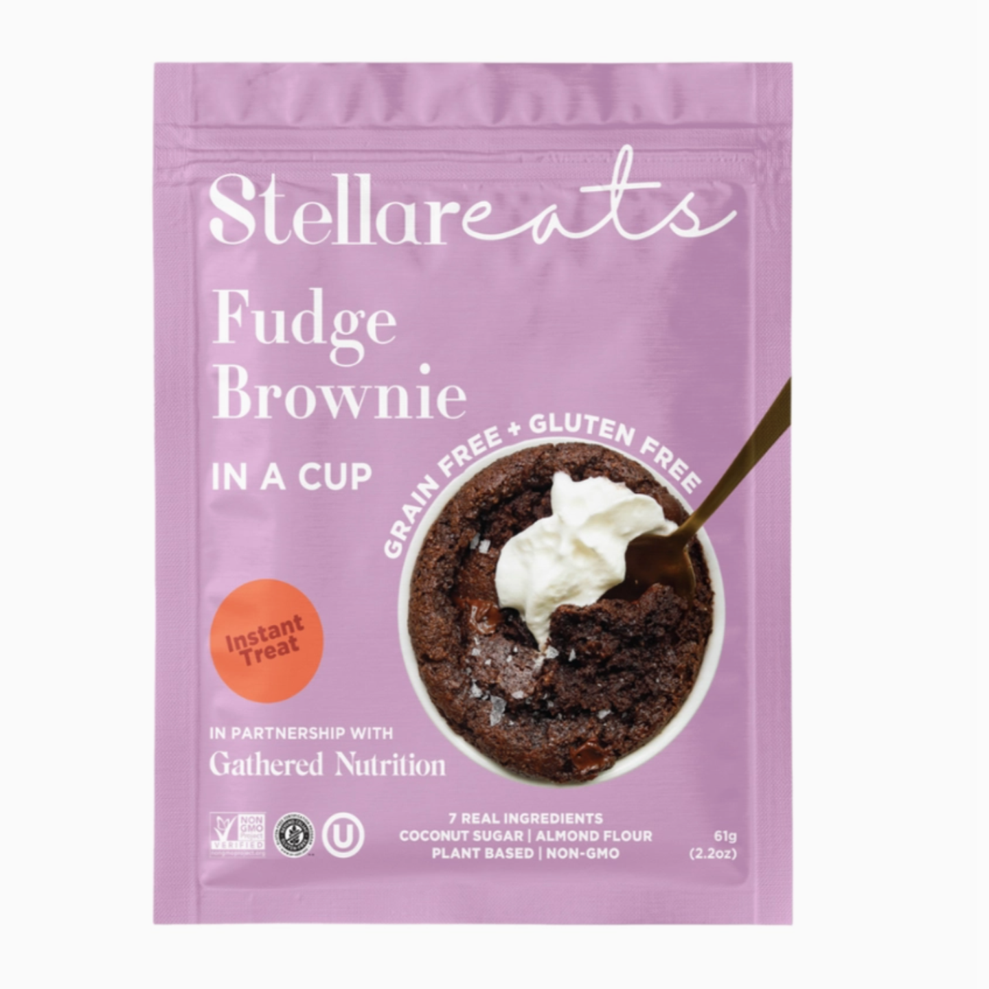 A lilac/pink/purple colored packet labeled "Stellar Eats Fudge Brownie In a Cup." The packaging highlights that it is "grain-free" and "gluten-free." A spoon is inserted into a rich-looking brownie topped with whipped cream. The label mentions "Instant Treat" and "7 Real Ingredients," listing coconut sugar, almond flour, plant-based, and non-GMO. It is in partnership with Gathered Nutrition.