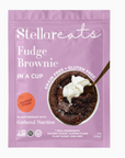 A lilac/pink/purple colored packet labeled "Stellar Eats Fudge Brownie In a Cup." The packaging highlights that it is "grain-free" and "gluten-free." A spoon is inserted into a rich-looking brownie topped with whipped cream. The label mentions "Instant Treat" and "7 Real Ingredients," listing coconut sugar, almond flour, plant-based, and non-GMO. It is in partnership with Gathered Nutrition.