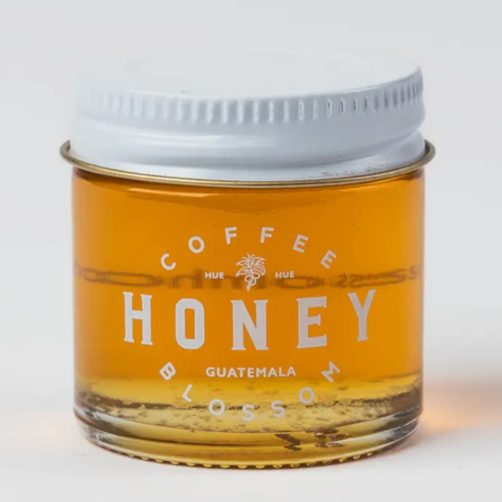 a small glass jar of honey with a white lid and the label "coffeeblossomhoney.com." The honey inside is a rich, golden color, and the design is simple and minimalist.