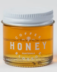 a small glass jar of honey with a white lid and the label "coffeeblossomhoney.com." The honey inside is a rich, golden color, and the design is simple and minimalist.