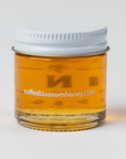  a small glass jar of honey with a white lid. This jar has a more elaborate label that reads "COFFEE BLOSSOM HONEY GUATEMALA" with decorative text and a small palm tree icon. The honey inside is similarly golden, and the label design is a bit more detailed, adding a stylish and artisanal feel to the product.