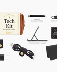 "Flat lay display of the brown 'Tech Kit for Taking Charge' by Pinch Provisions, showing its 8 included items: an earbud cleaning tool, webcam cover, phone/tablet stand, password cheat sheet, microfiber cleaning cloth, USB charging cable with multiple connectors, wall adapter, and a cord organizer. The items are neatly arranged on a white background for a clear and organized presentation.