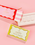 MUSEE MERRY CHRISTMAS SOAP WITH PINK AND WHITE STRIPED PACKAGING NEXT TO THE HAPPY HOLIDAYS SOAP