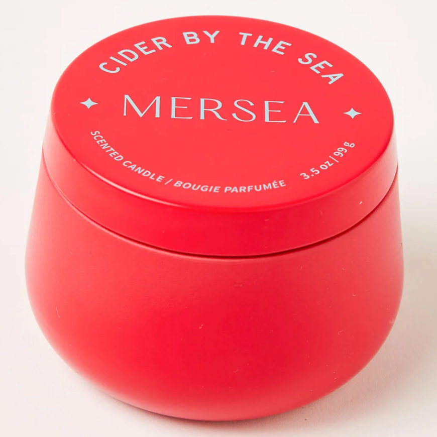 RED TIN CANDLE THAT READS, "CIDER BY THE SEA, MERSEA, SCENTED CANDLE" IN LIGHT BLUE WRITING