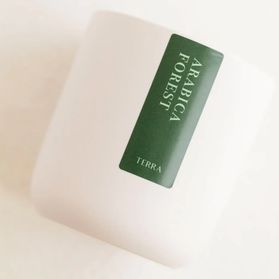 WHITE CANDLE WITH A GREEN LABEL THAT SAYS ARABICA FOREST BY TERRA
