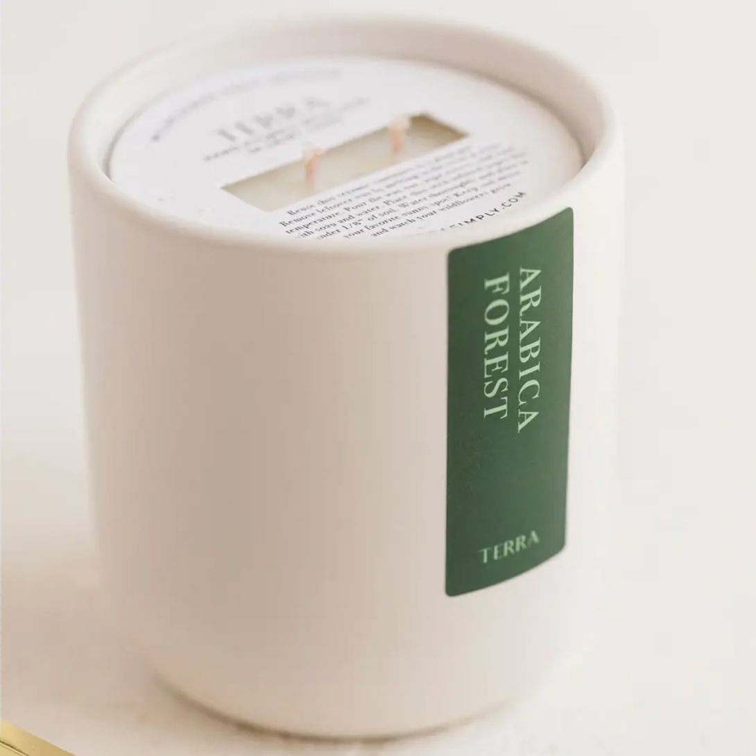 WHITE CANDLE WITH A GREEN LABEL THAT SAYS ARABICA FOREST BY TERRA, SHOWN STANDING UP