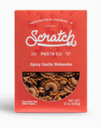 A boxed pasta product labeled "Scratch Pasta Co" in red packaging. The flavor is "Spicy Garlic Mohawks," featuring a small window displaying the uniquely shaped pasta inside. The packaging mentions that it is handcrafted and made with garlic and spices, weighing 12 ounces (430g).