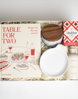 Table for Two ready to ship in creme featuring "Table for Two" cookbook, Le Creuset spoon rest, Branche olive oil, Maldon Chili Salt, and marble salt cellar