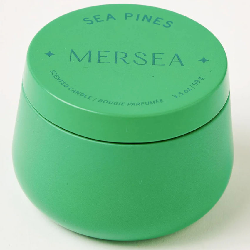 GREEN TIN CANDLE THAT READS IN BLUE WRITING "SEA PINES / MERSEA/ SCENTED CANDLE BOUGIE PARFUMEE 3.5OZ, 99G" ON A WHITE BACKGROUND