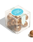 Clear cube box with gold truffles and a blue label on a white background