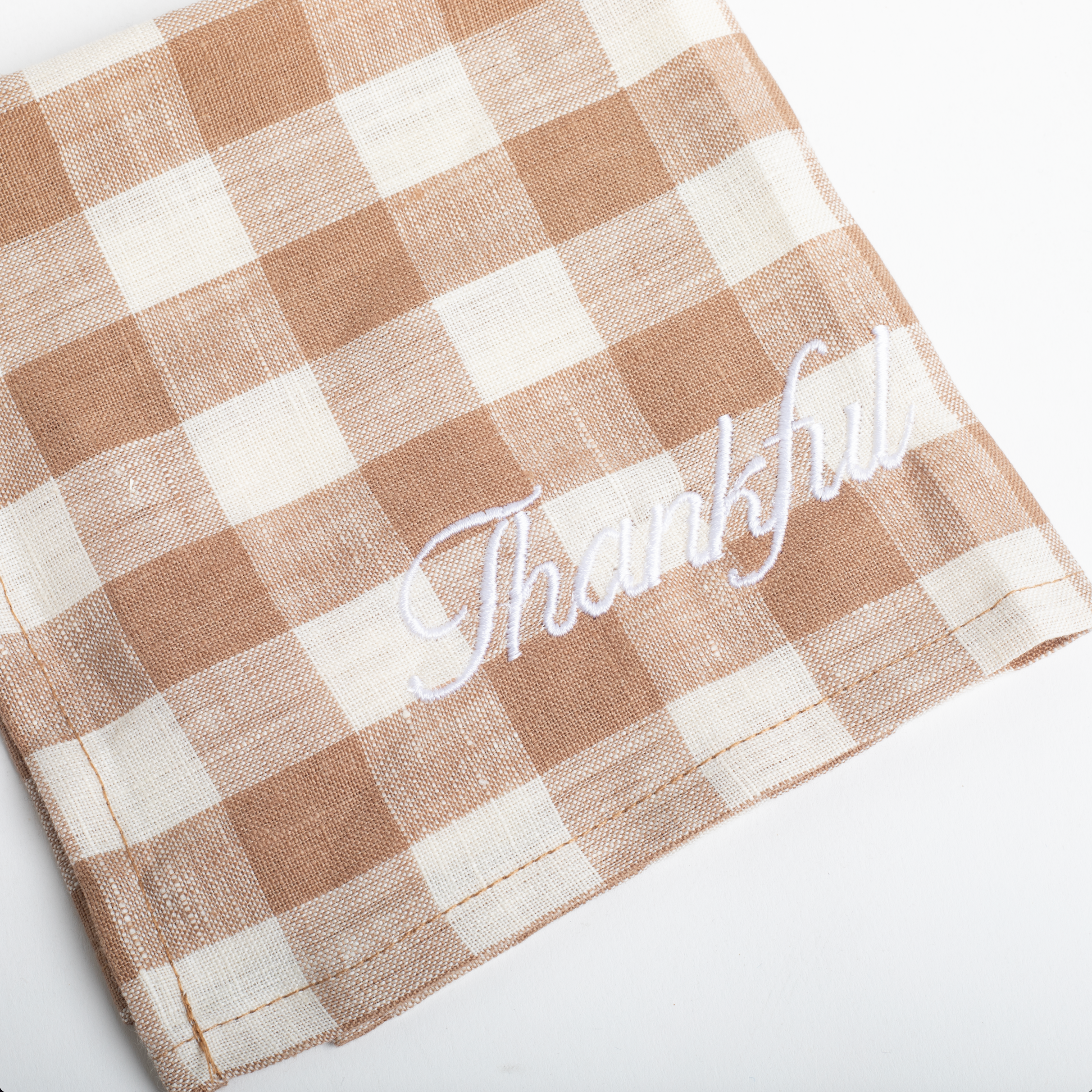 Checkered napkin with 'Thankful' embroidery on a white background