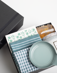 Gift set with a mug, towel, and other items in a black box on a white background