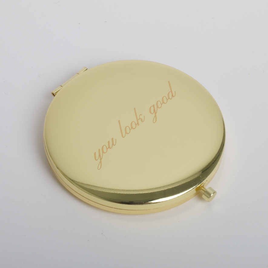 Round gold compact mirror with 'You look good' text on a light gray background