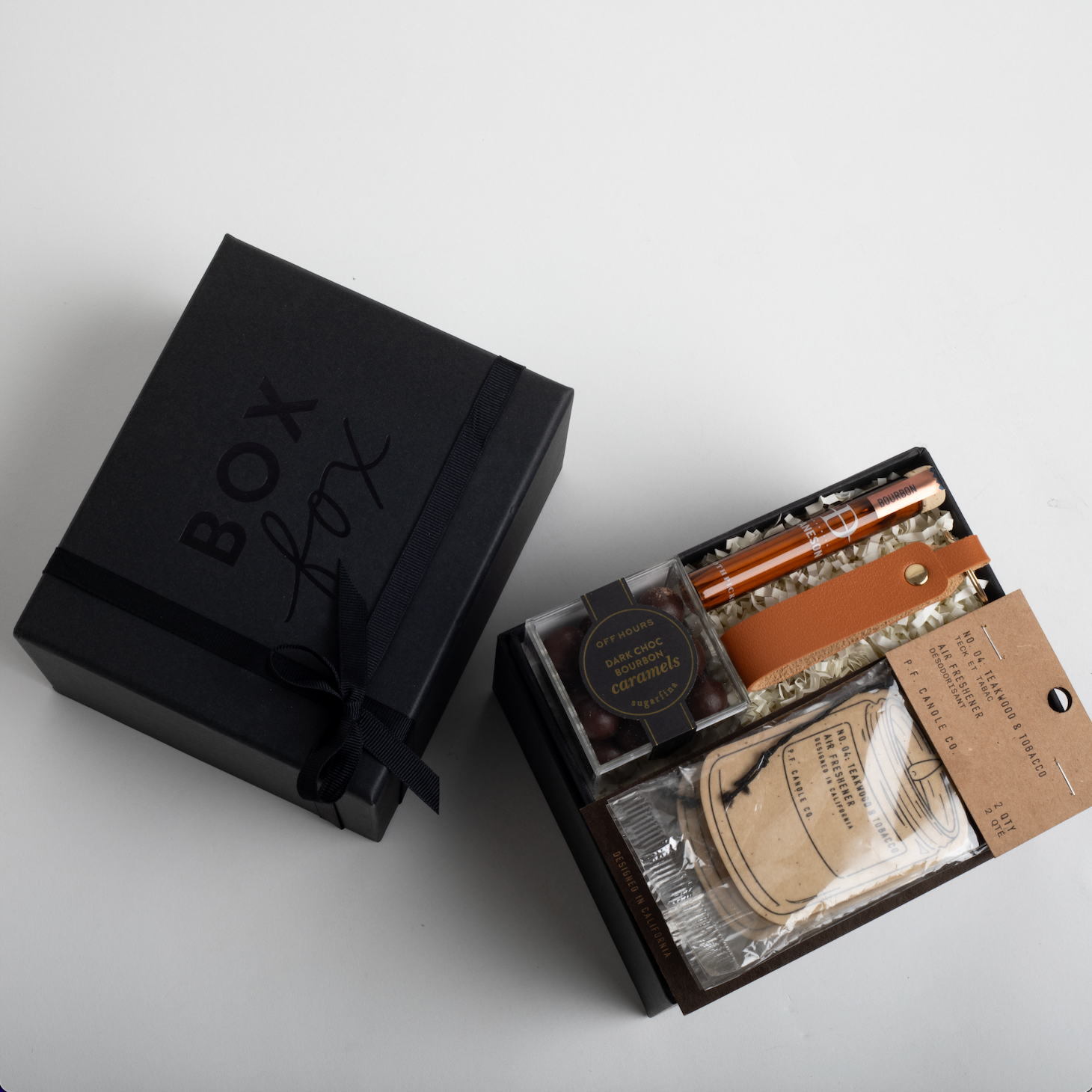 Open black gift box with various items on a light gray background