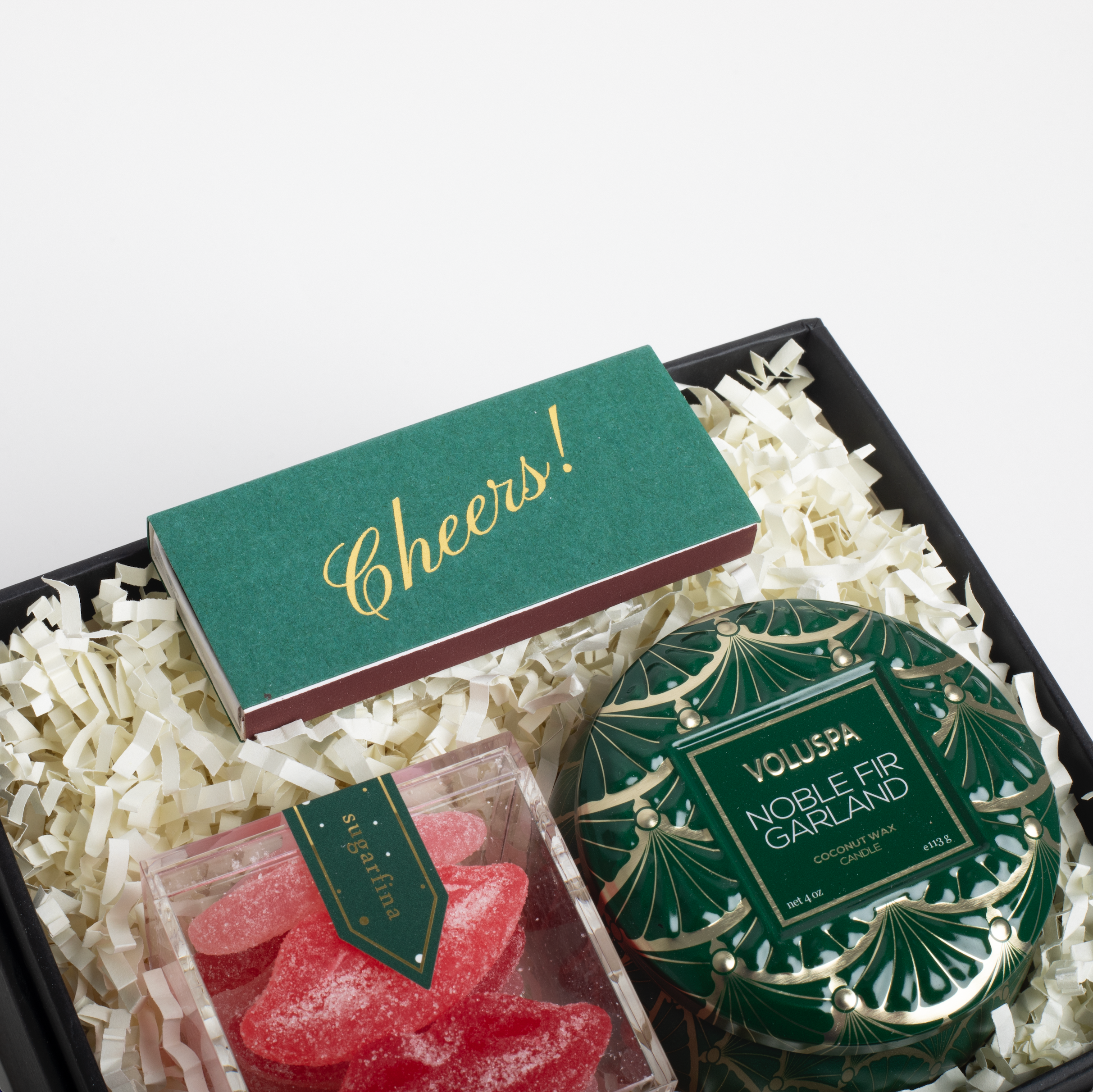 Gift set with a green box labeled &#39;Cheers!&#39;, a decorative garland, and red candy hearts on a white background.