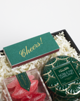 Gift set with a green box labeled 'Cheers!', a decorative garland, and red candy hearts on a white background.