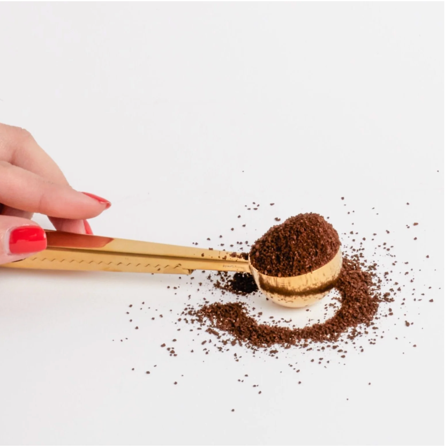 Hand holding a gold scoop filled with coffee grounds on a white background
