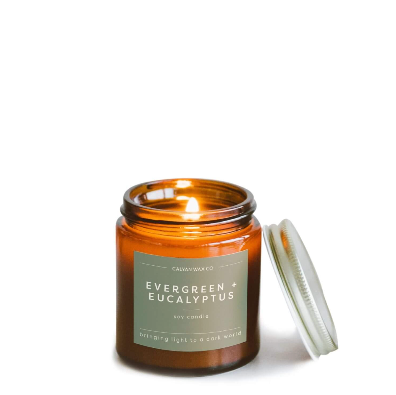 Brown candle jar with lit flame and green label with tin lid resting next to it
