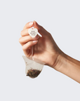 Hand holding a tea bag with 'Bio Heart Teas' label against a light background