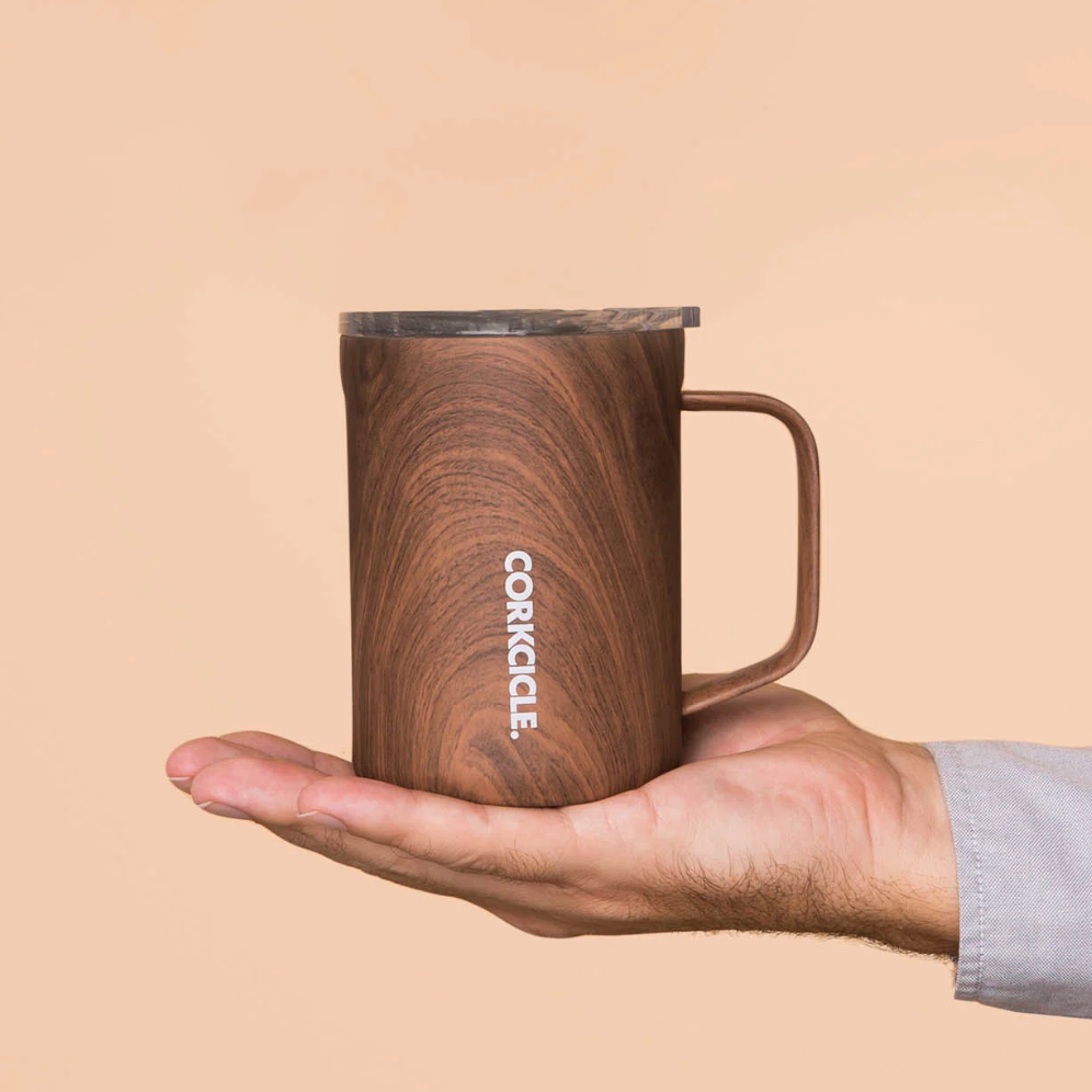 Hand holding a wooden-patterned mug with 'Corkcicle' branding against a beige background