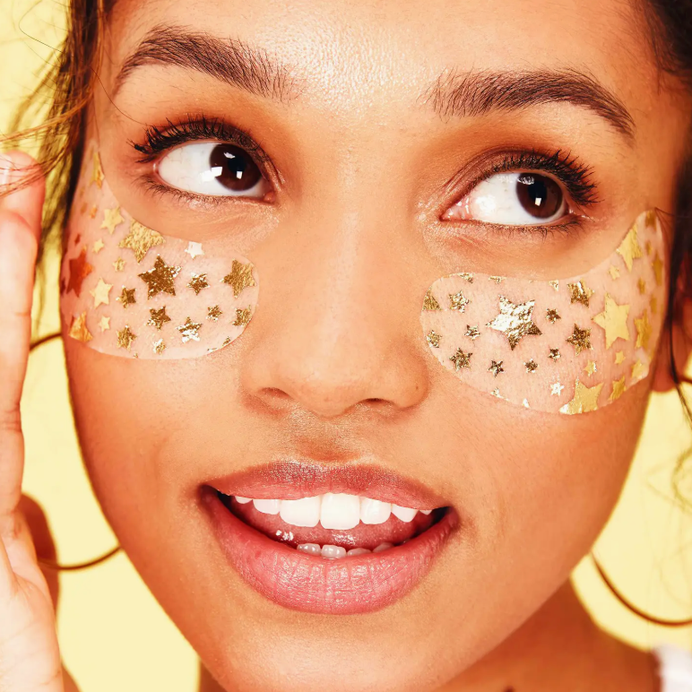 Woman wearing gold star-shaped eye patches with a blurred yellow background