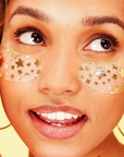Woman wearing gold star-shaped eye patches with a blurred yellow background