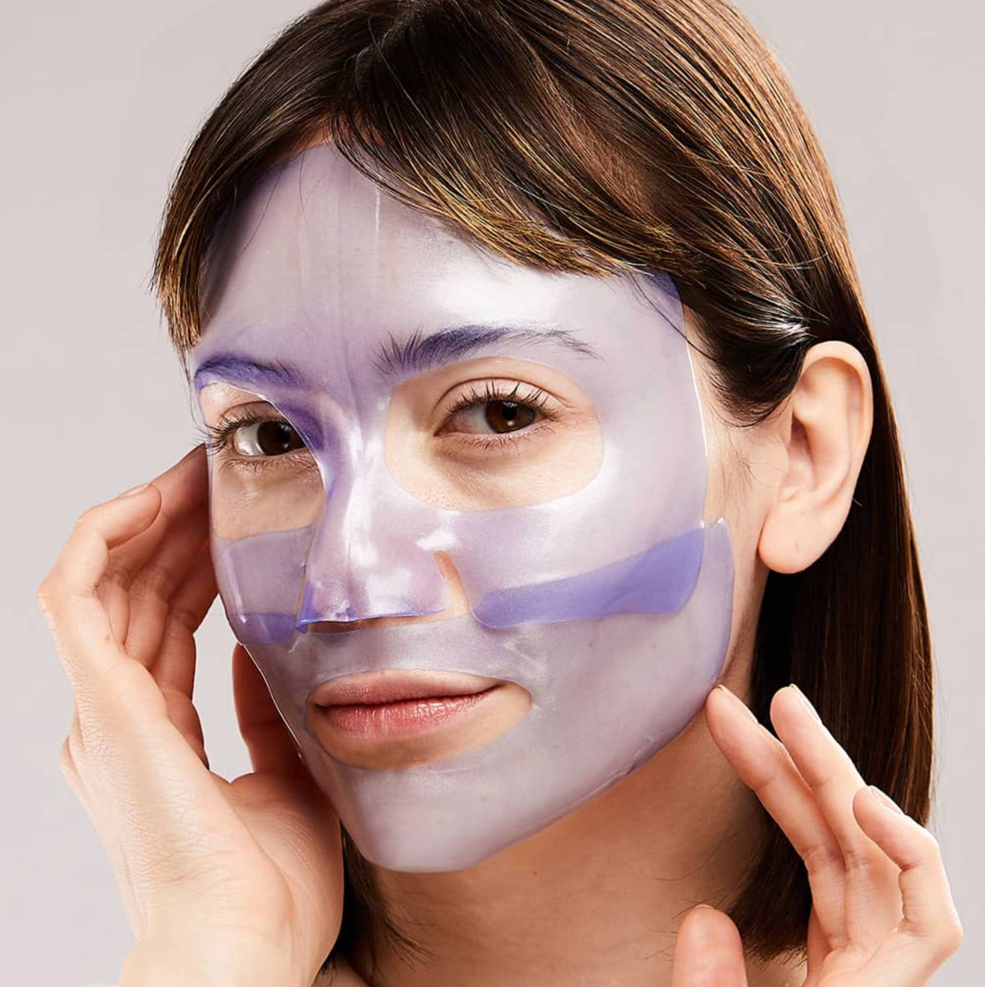 Woman applying a purple facial mask on a plain background