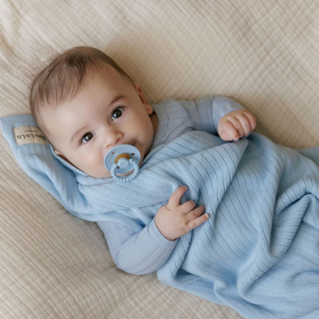 Baby wrapped in a blue swaddle with a pacifier, lying on a textured surface.