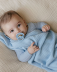 Baby wrapped in a blue swaddle with a pacifier, lying on a textured surface.