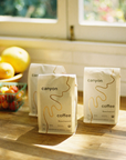 Canyon Coffee bags on a wooden surface with a window and fruit in the background