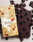 Dark chocolate bar with cherry vanilla flavor packaging surrounded by dark chocolate pieces on a light background