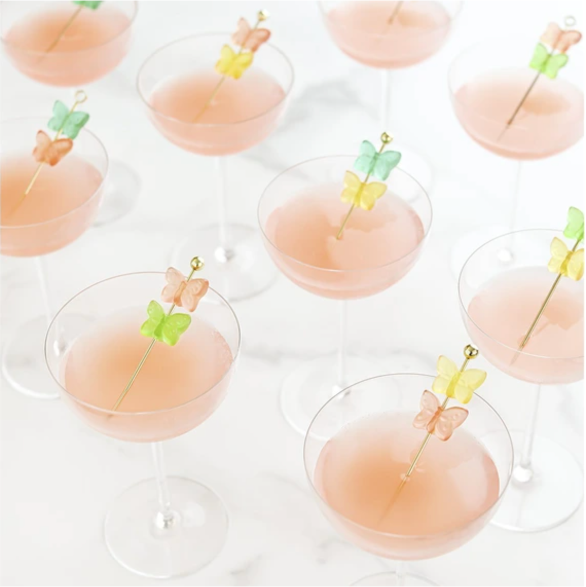 Cocktail glasses with pink liquid and butterfly cocktail picks on a white background