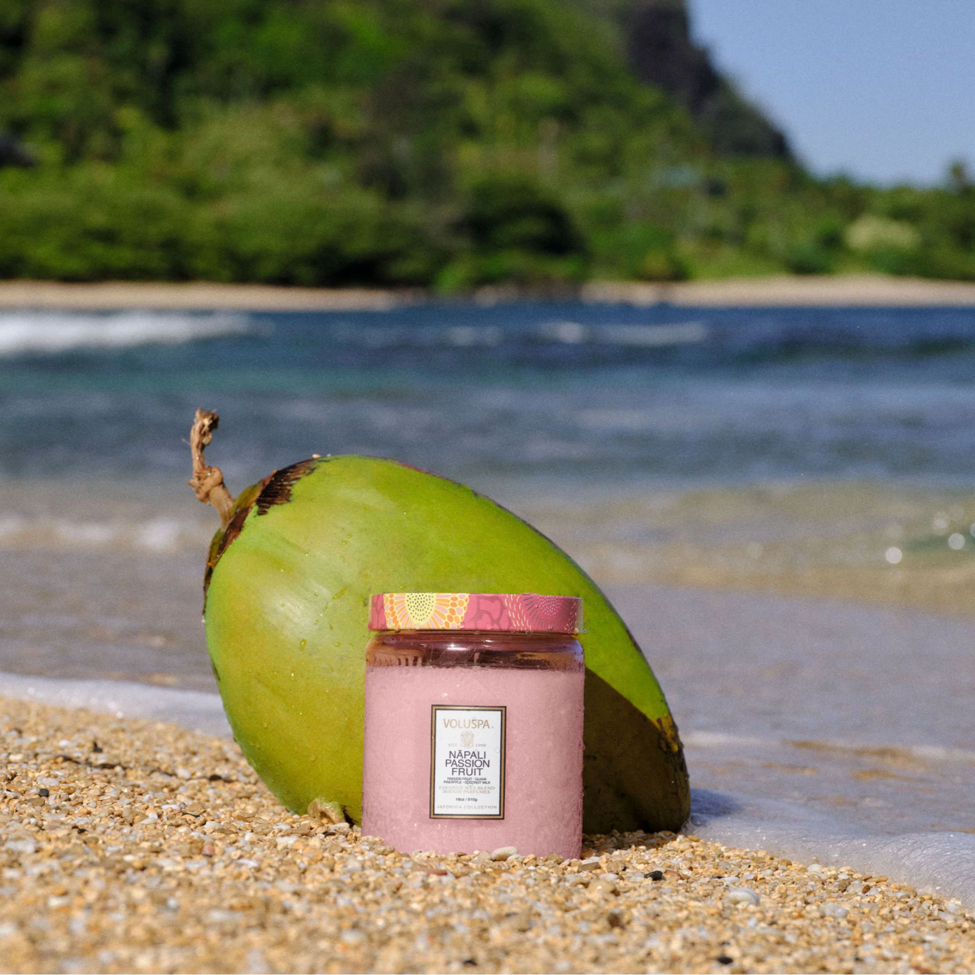 Candle in a pink container with a green coconut on a beach